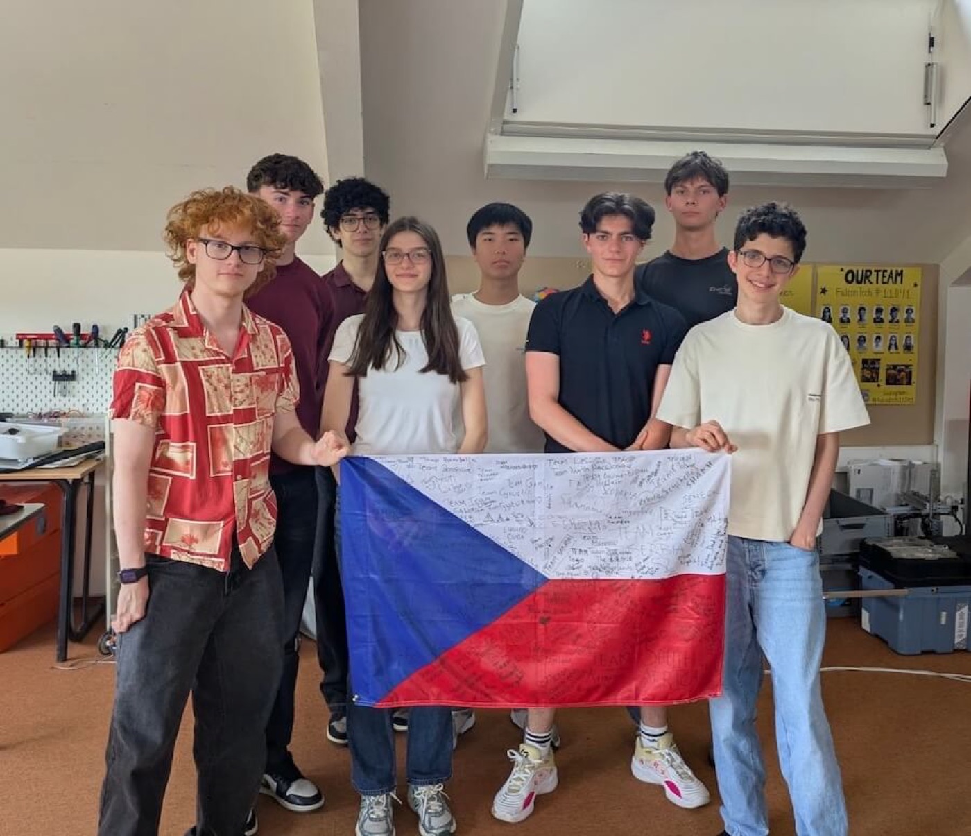 Team Czechia 2026 holding a signed Czech flag in the robotics lab